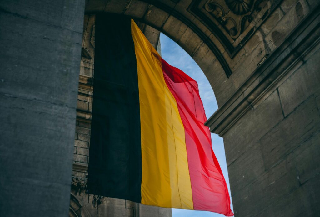 Belgian flag waving under a stone arch in Brussels, symbolising moving to Belgium with VANonsite European removals