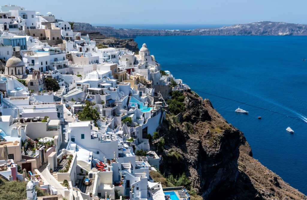 Whitewashed cliffside town overlooking a deep blue sea, with boats in the water and rocky coastline in the distance