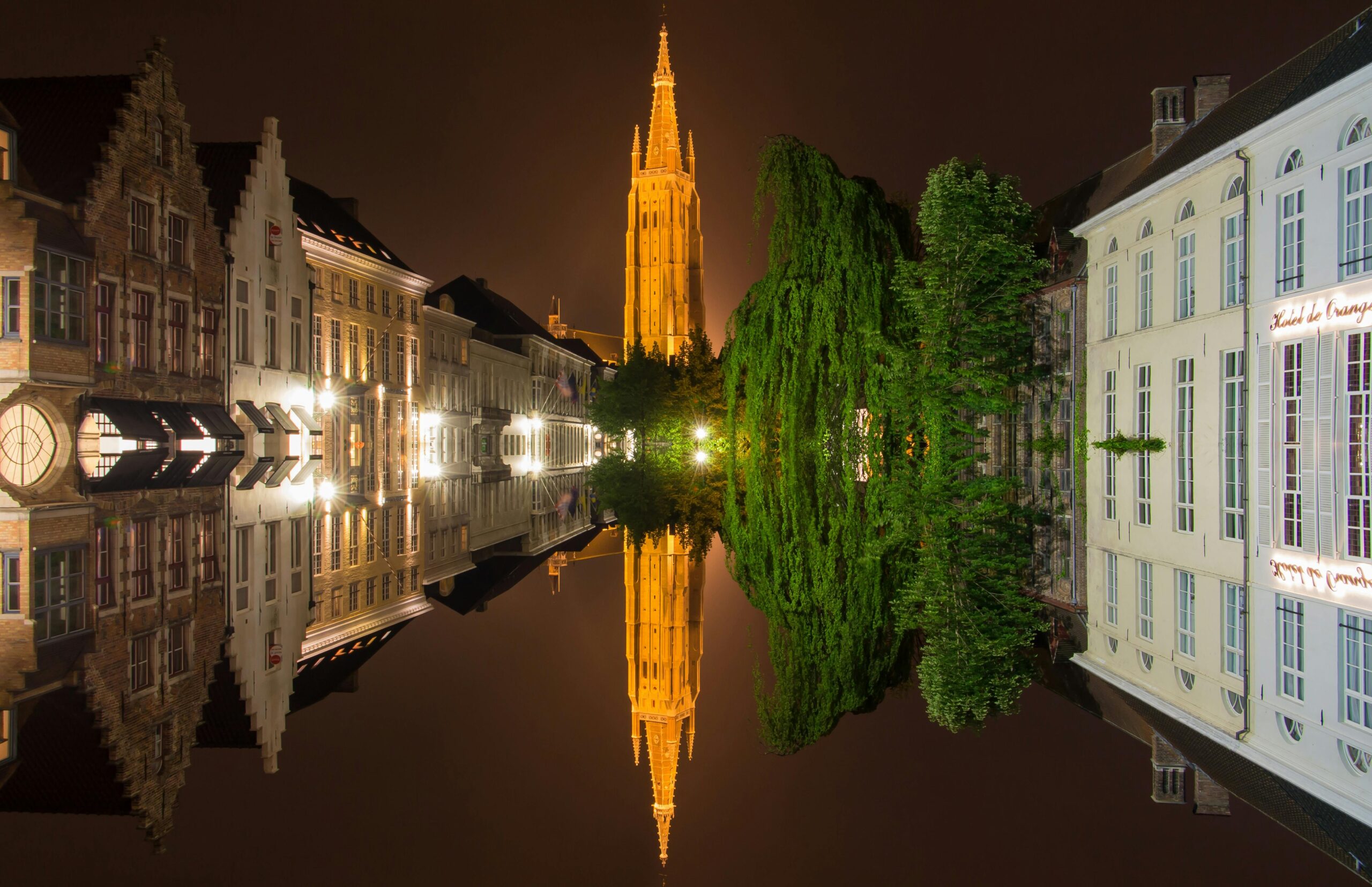 Night view of Bruges canal with illuminated Church of Our Lady and historic Belgian houses reflected in the water, showing the charm of moving to Belgium with VANonsite European removals
