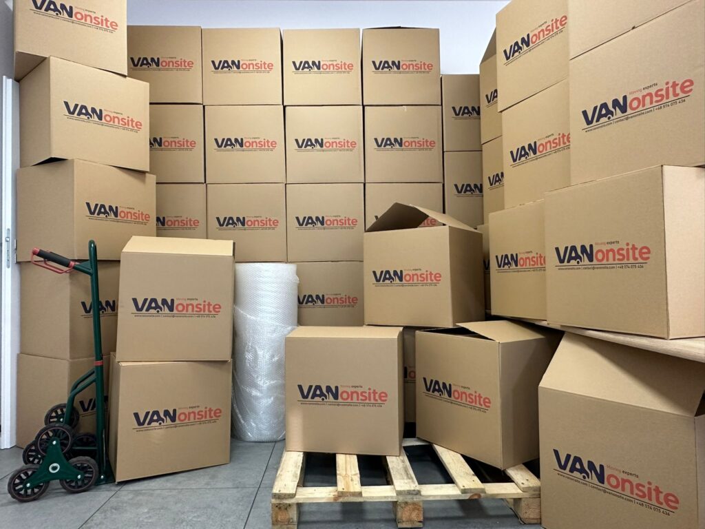 Stack of branded VANonsite moving boxes with trolley and packing materials prepared for European removals and international moving services