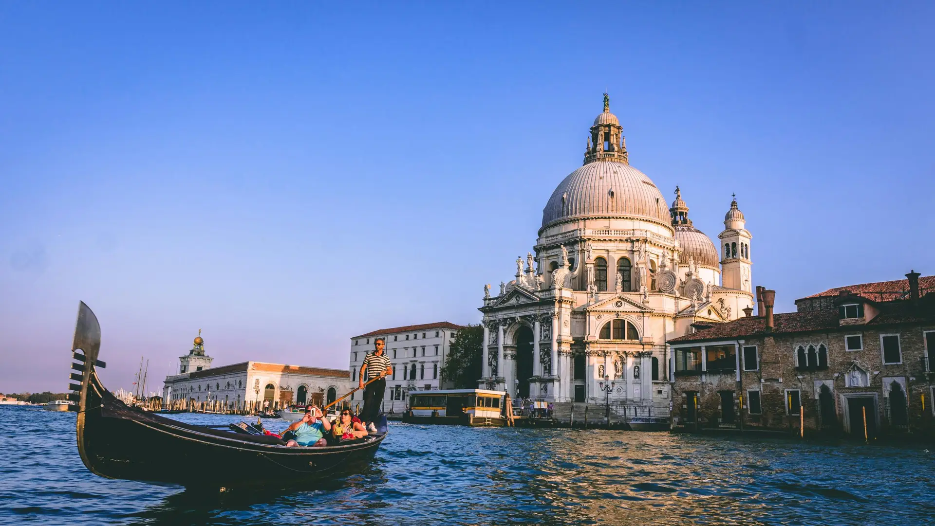 Family enjoying a gondola ride in Venice with historic church in the background, symbolising stress free removals to Italy and European relocations with VANonsite