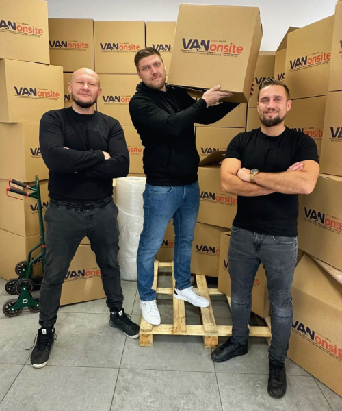 Three VANonsite team members in a warehouse surrounded by branded moving boxes, one holding a box for packing